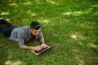 Sakallı tasarımcısında yakışıklı: casual giyim ile yardım etmek-in laptop, portre vurdu başlangıç proje üzerinde çalışırken yeşil çim üzerinde yalan