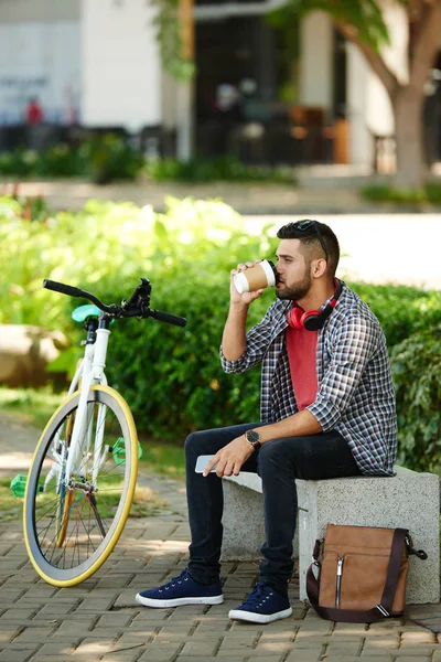 自信的胡子骑自行车坐在公园长椅上 享受芳香的咖啡 而采取短暂休息 全长肖像 — 图库照片