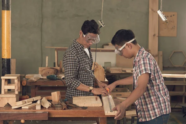 son and father carpenters working with wood in workshop, measuring wooden plank