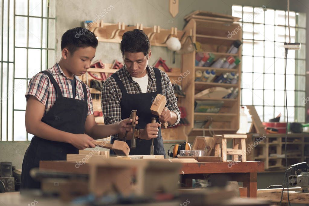 Vietnamese teenage boy helping his father in workshop