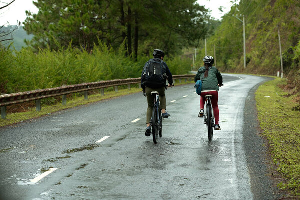 Rear view of couple cycling together down wet road 