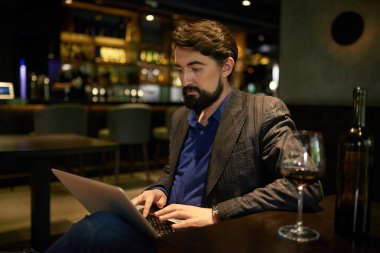 dizüstü bilgisayarda çalışan ve kırmızı şarap cam restoran barda ile masada oturan sakallı 