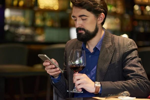 Businessman resting with glass of wine and smartphone