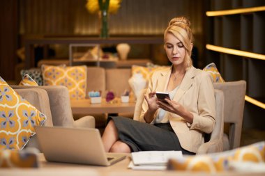 Sarışın iş Bayan okuma iletisi koltuk üzerinde otel lobisinde otururken smartphone içinde 