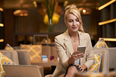 Divan Otel lobisinde otururken çekici Bayan okuma mesaj smartphone içinde gülümseyen 