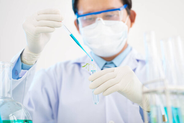 scientist man wearing white coat and safety goggles carrying out experiment with genetically modified sprout