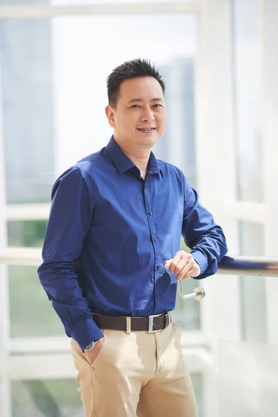 Portrait of cheerful asian businessman standing at window