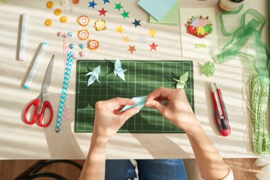 ahşap masada otururken yukarıdan tanınmaz halde kadının origami yapma vinç