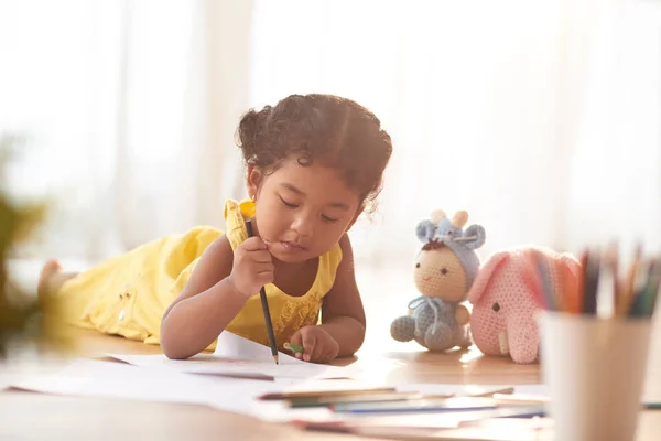 かわいい女の子のおもちゃで床の上に横たわると 鉛筆で紙に描画 — ストック写真