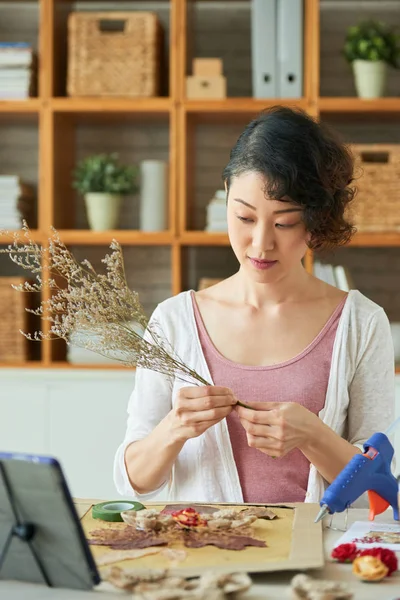 Pretty Japanese woman glueing dry flowers on picture