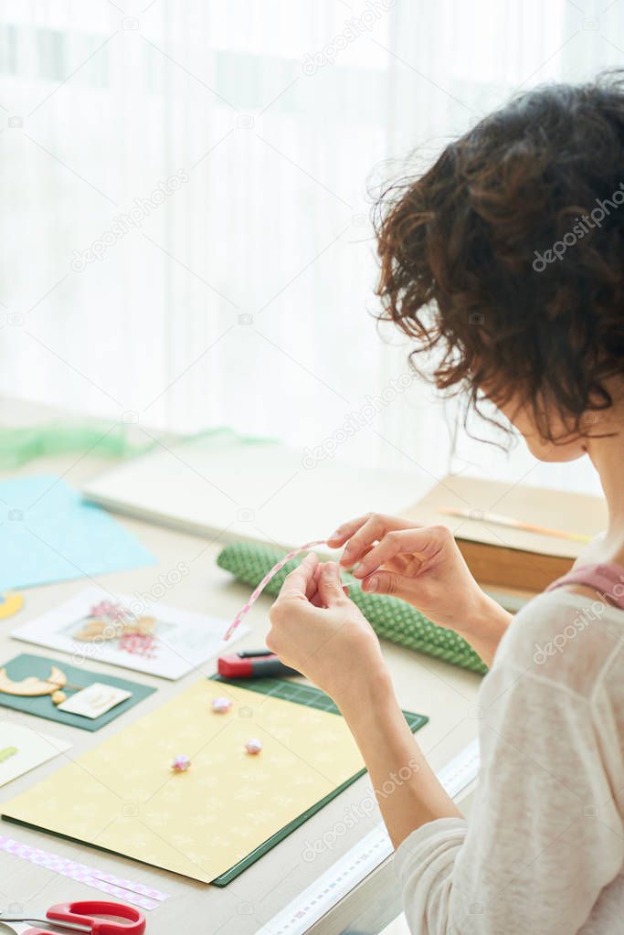 Profile view of curly woman sitting at wooden table while enjoying process of handmade greeting card creation