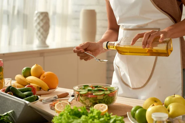モダンなキッチンに立っている野菜サラダにオリーブ油を注ぐをエプロン雌性食べ物ブロガーを着て — ストック写真