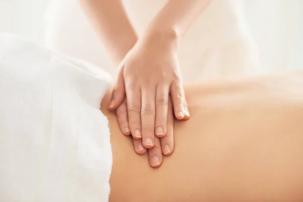 Crop hands of female therapist rubbing loin of female client during massage session in spa salon