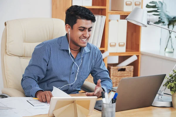 Cheerful Indian man working and communicating with laptop in office