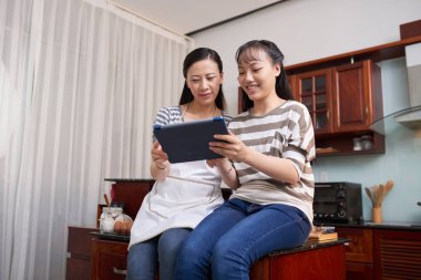 Mutfak tezgahına oturma ve yemek pişirme önce tarifi dijital tablet izlerken genç güzel Asian Kız