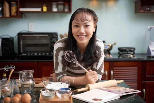 年轻漂亮的亚洲女人拿着炊具站在厨房柜台前 拿着威士忌 高兴地对着镜头微笑的肖像 — 图库照片