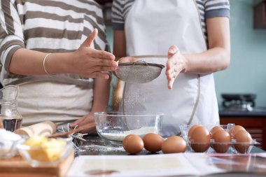 Mutfak tezgahı tarafından ayakta ve kurabiye hamuru yaparken elek un eleme tanınmaz halde kadınların düşük açılı görünüş