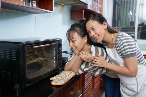 年轻漂亮的亚洲母女和女儿站在家里的厨房里看着烤箱 那里的饼干被烤着 笑得很开心 — 图库照片