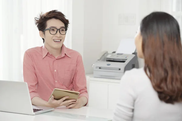 年轻的亚洲男子拿着眼镜拿着平板电脑 在办公室的桌子上与同事的女人交谈 — 图库照片