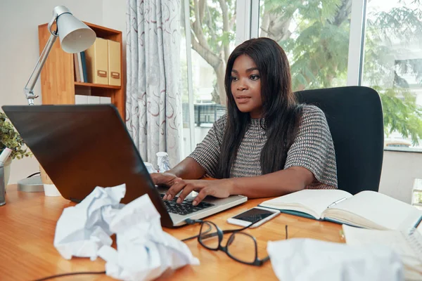 成人美丽的黑人妇女使用笔记本电脑在桌子上的文件和记事本努力工作 — 图库照片