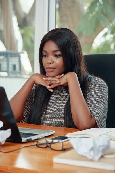 现代成年黑人妇女在办公室的桌子上工作 一边靠在手上看着笔记本电脑 — 图库照片