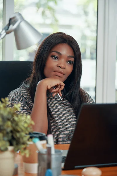 美丽的黑人妇女看着笔记本电脑沉思地工作在桌子在现代办公室 — 图库照片