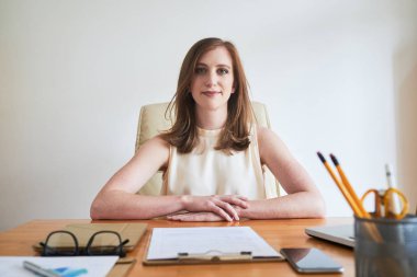 Genç kadın ofiste beyaz duvar karşı masada otururken kameraya bakarak içerik