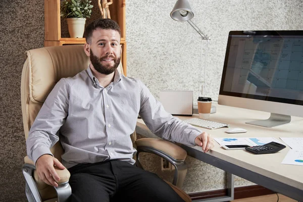 彼のオフィスのテーブルに座って満足して興奮している実業家 — ストック写真