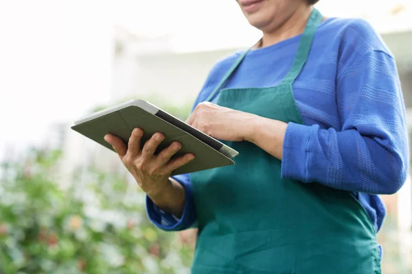 屋外立ちながら作業でデジタル タブレットを使用エプロンで成熟した女性庭師のクローズ アップ — ストック写真