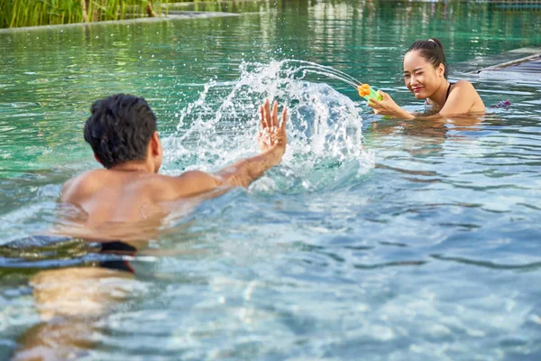 年轻的亚洲夫妇在游泳池里玩水枪 — 图库照片