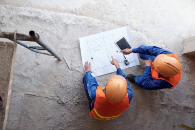 İnşaat yöneticileri turuncu kavganın blueprint yere işaret içinde görüntülemek yukarıdan