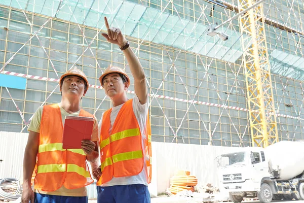 Twee Vietnamese Bouwvakkers Helder Oranje Vesten Hardhats Bespreken Werk — Stockfoto