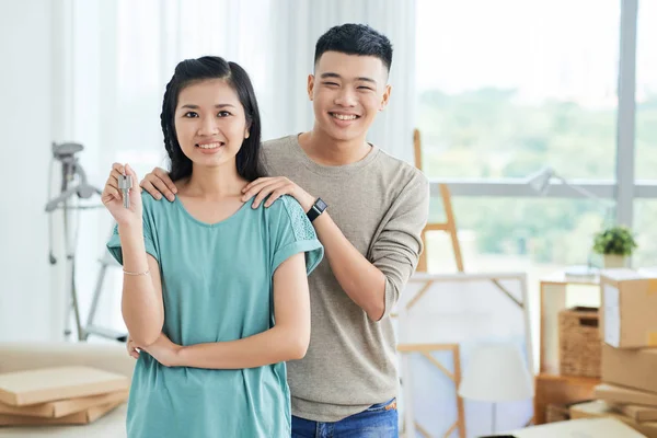 陽気な若い美しいアジアの女性は新しい家にキーを示し 彼女の肩に手を繋いでいる近くに立っている人を笑顔 — ストック写真
