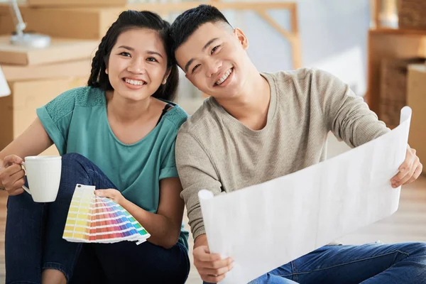 美しい陽気なアジア男と女のカップと色パレットを保持している新しいアパートの床に座って — ストック写真