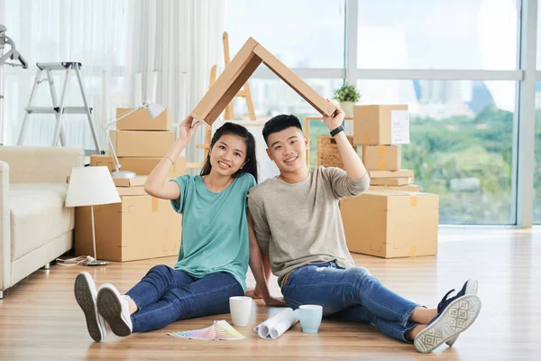 young Asian man and woman sitting on floor of new apartment