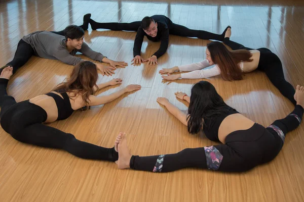 Group of young Asian people bending forward and stretching while sitting in circle on timber floor in dance studio