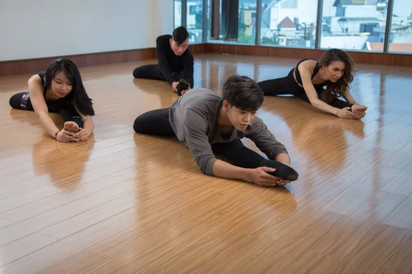 Young Asian people sitting on wooden floor and stretching body during dance practice in studio