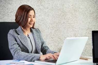 Masasında oturan ve iş dizüstü bilgisayar kullanmaktan gülümseyen ofis çalışanı