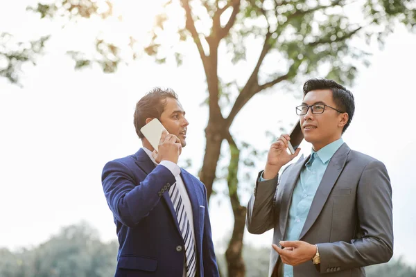 Dwóch Konsultantów Garniturach Omawiając Coś Telefon Komórkowy Stojąc Zewnątrz — Zdjęcie stockowe