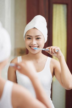 Yansıma diş diş fırçası ayakta ayna önünde ile temizlik havlu içinde gülümseyen Asyalı kadın