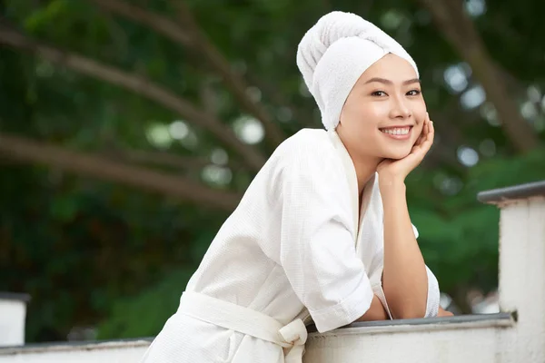 白いタオルでカメラに笑顔のシャワー後テラスで新鮮なバスローブ立っている純粋なアジア女性をコンテンツします — ストック写真