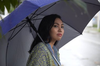 Side view of beautiful Filipino woman with umbrella looking away while standing on street on rainy day