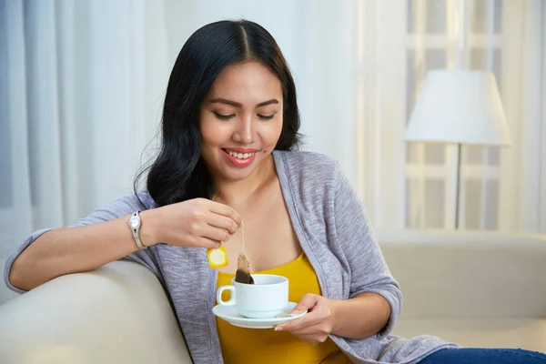 Attractive Filipino Woman Smiling Dipping Tea Bag Cup While Sitting — Stok fotoğraf
