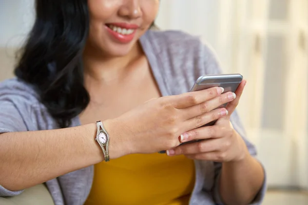 无法辨认的菲律宾女士微笑和浏览现代智能手机 而靠在时尚的客厅的沙发上 — 图库照片