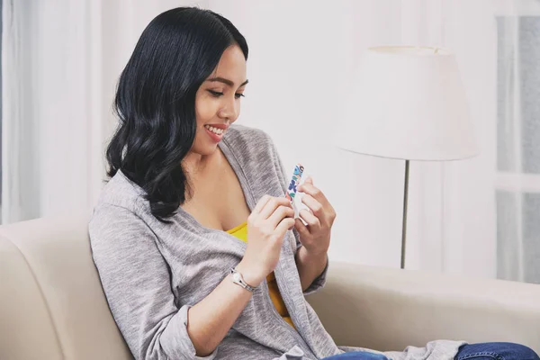 Lovely Filipino Female Smiling Filing Fingernails While Relaxing Comfortable Sofa — стокове фото