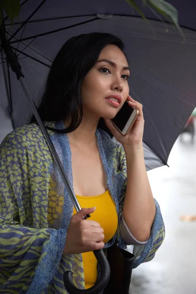 有吸引力的菲律宾妇女与伞说话的智能手机和看着离开 而站在城市街道上 在雨天 — 图库照片