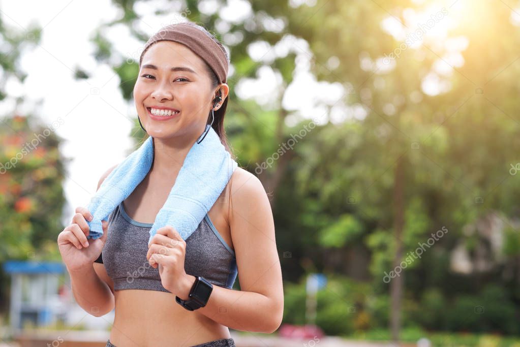 Young Asian woman in headband and sportswear smiling at camera in park