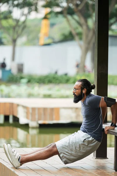 在户外锻炼时 通过耳塞听音乐的印度男性运动员的侧视图 — 图库照片