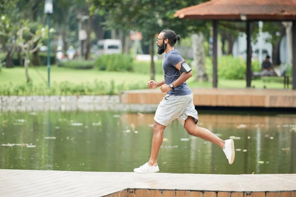 运动胡子印度男子与智能手机在户外慢跑和听音乐通过耳塞侧视图 — 图库照片