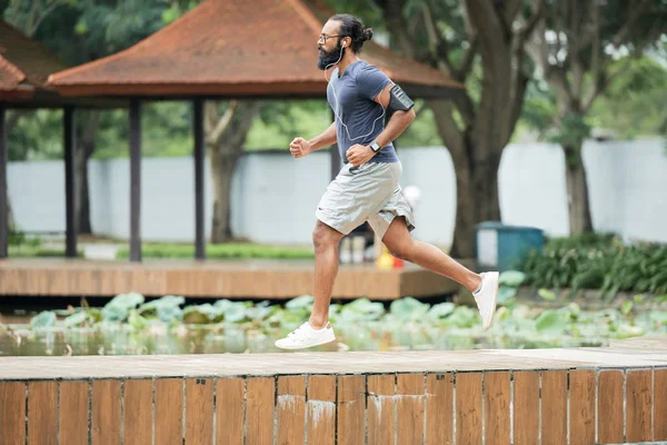 公園を走っていると イヤホンで音楽を聴く長いひげと筋肉インド男性アスリートの側面図 — ストック写真